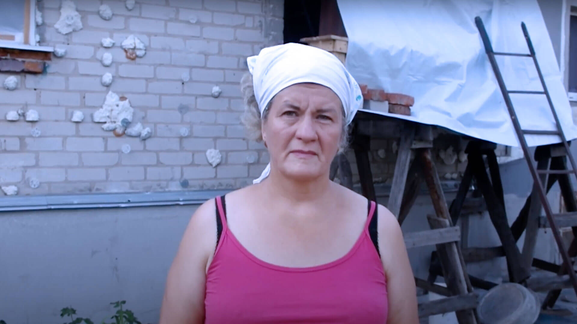 Woman in headscarf stands outside her damaged home in Ukraine