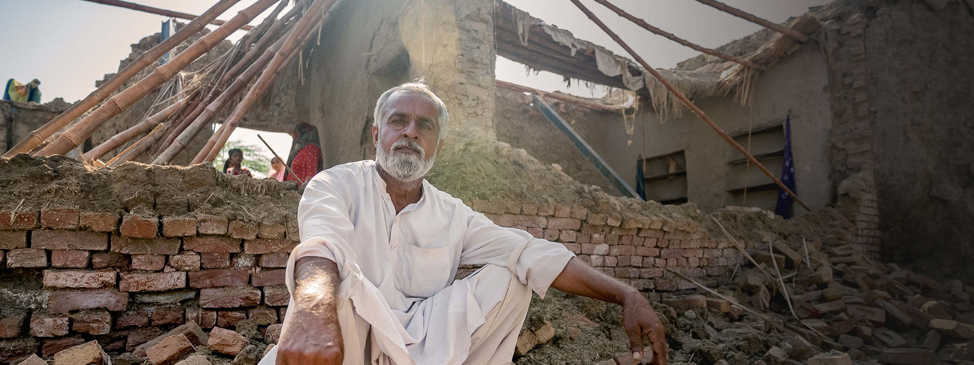 Man in Pakistan crouches outside his home destroyed by flooding