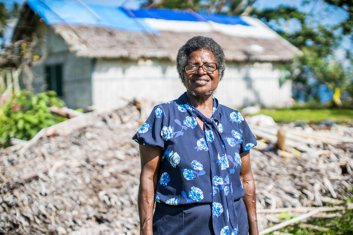 Lady smiling outside of a wall and a repaired home in Vanatau