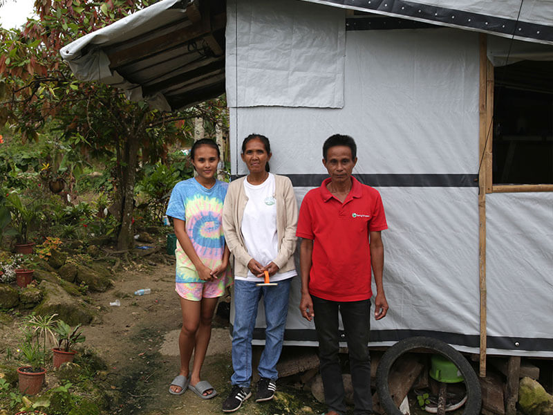 Filippino family stand proudly outside their emergency shelter after typhoon rai
