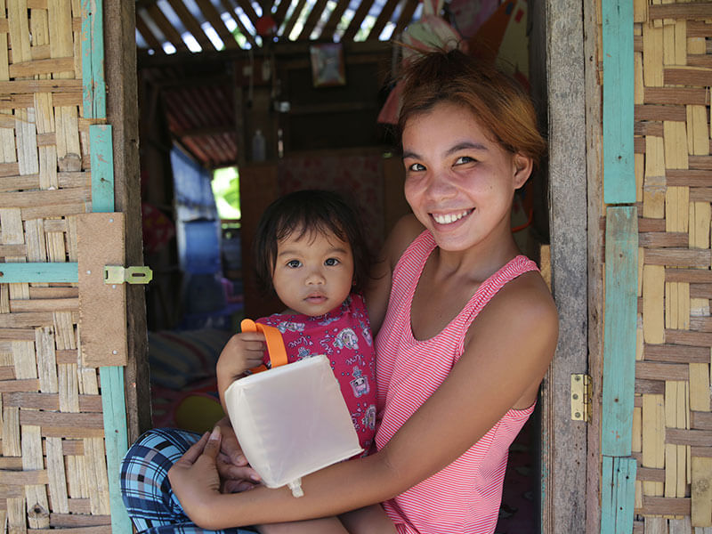 Young Filippino woman holds daughter and solar light in entryway of shelter