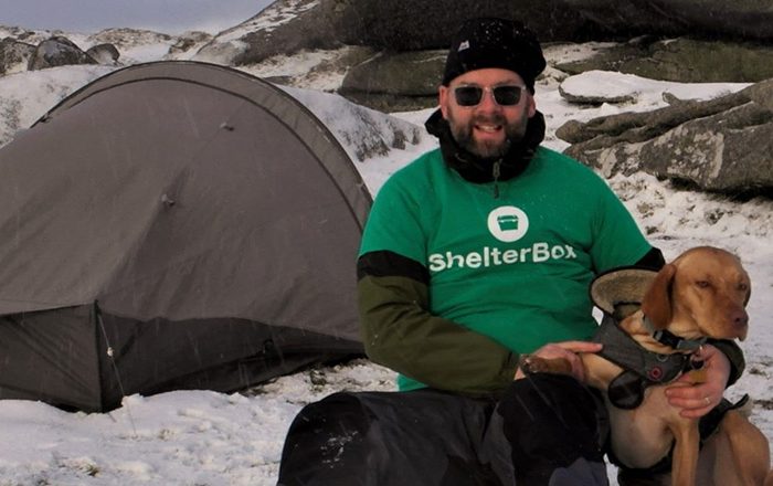 Man sitting outside in the snow next to a tent with his dog