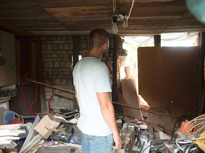 Ukrainian man in grey tshirt with his back to the camera looks at damage to his property after bombing