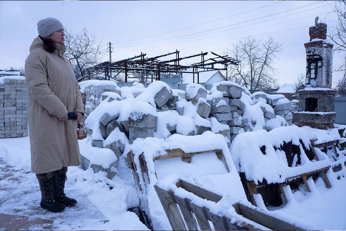 Woman looking at the remains of a collapsed house which is covered in snow