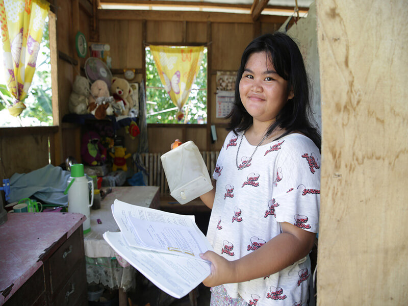 A young woman holding a solar light and her homework, smiling at the camera