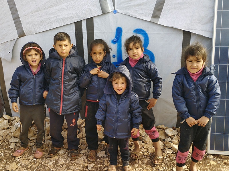 Six Syrian children smiling in blue winter coats