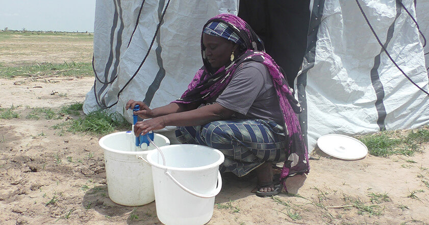 A woman sitting outside her tent in Cameroon, filtering water with a water filter