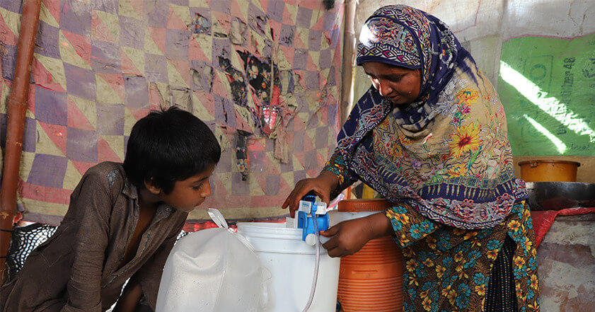 A woman and her son in their shelter filtering water with a water filter
