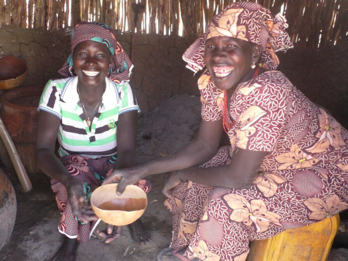 Two women sitting in a house in Cameroon smiling at the camera