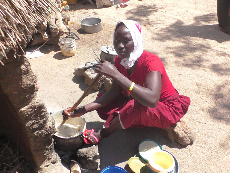 A woman sitting outside on the ground, preparing food for her family