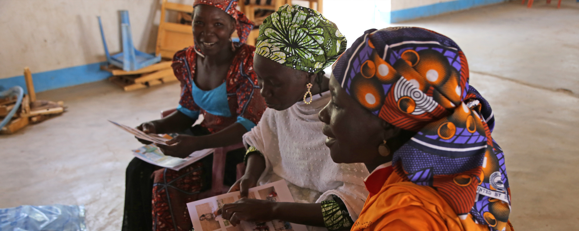 Three women in Cameroon sitting and looking at paperwork featuring their stories as part of ethical storytelling work