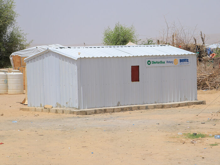 An iron net shelter made from corrugated steel on a concrete base standing on a sandy floor