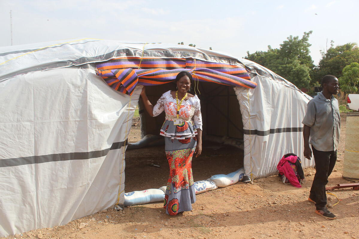 Lady standing in front of a large tent with a curved roof, covered with tarpaulins