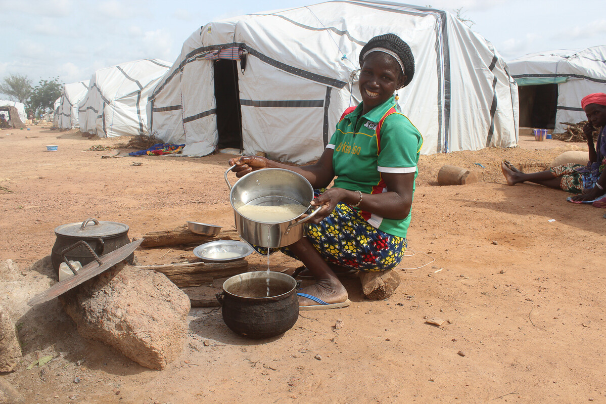 Lady crouching outside a tent and pouring food from a pot