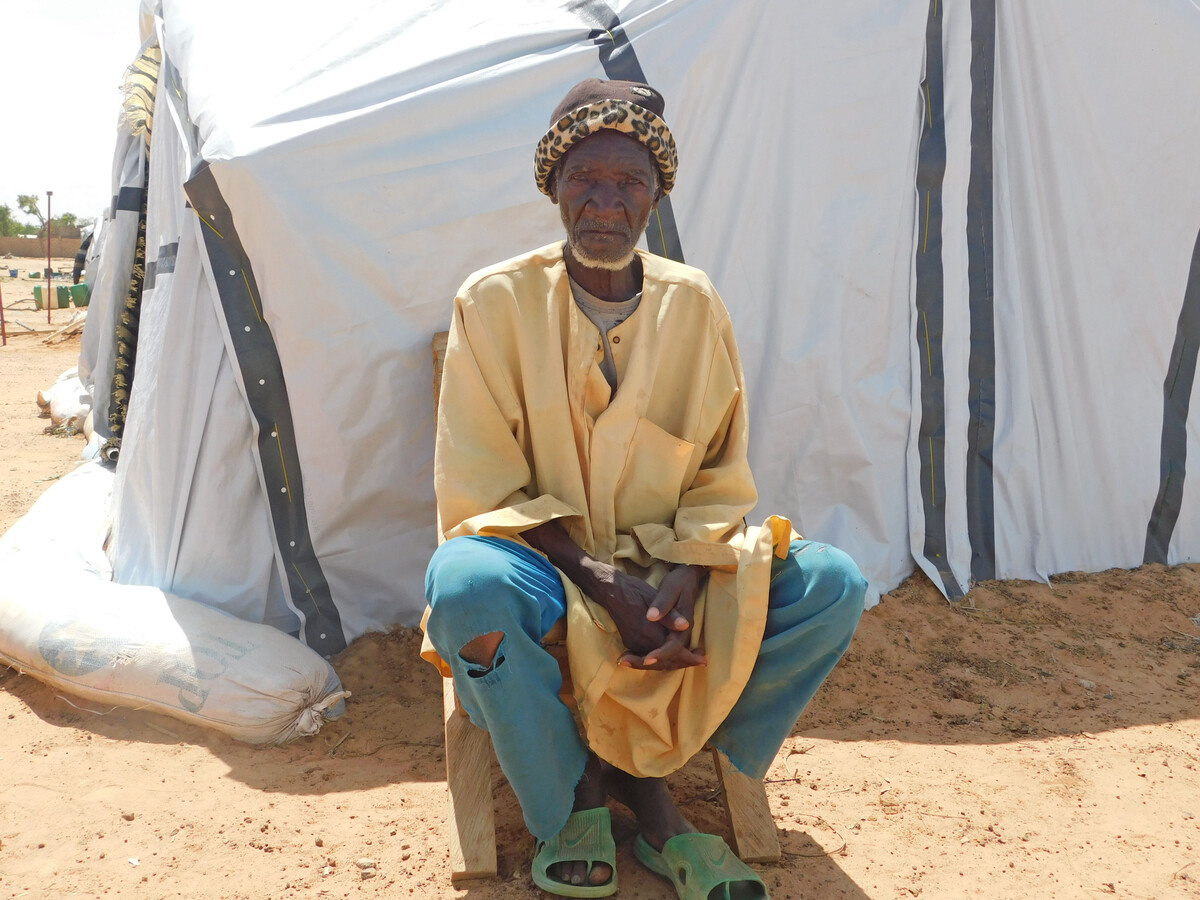 Man wearing yellow and blue sitting outside a tent
