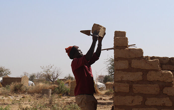 Man adding brick to a partially built building in Cameroon