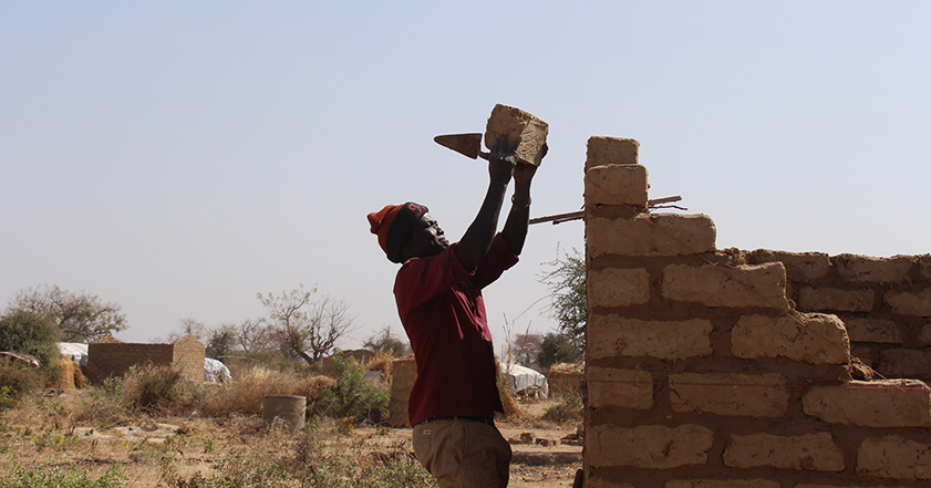 Man adding brick to a partially built building in Cameroon