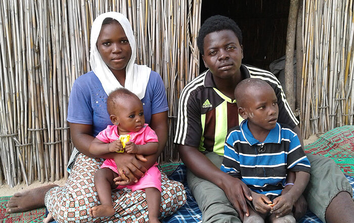 Man, woman and two babies sitting in front of a shelter
