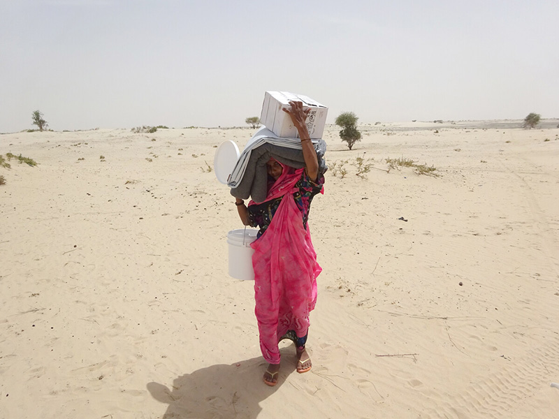 Lady carrying blankets and other items through a sandy desert