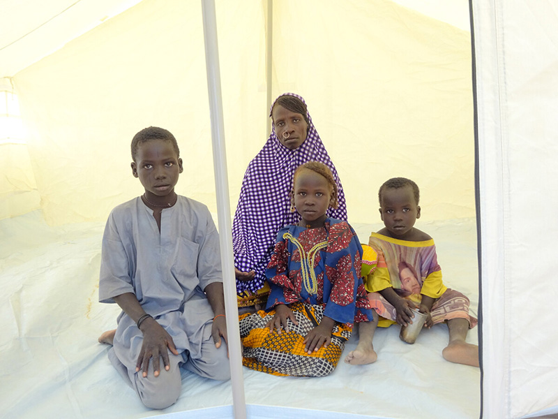 Mother and three children sitting inside a tent