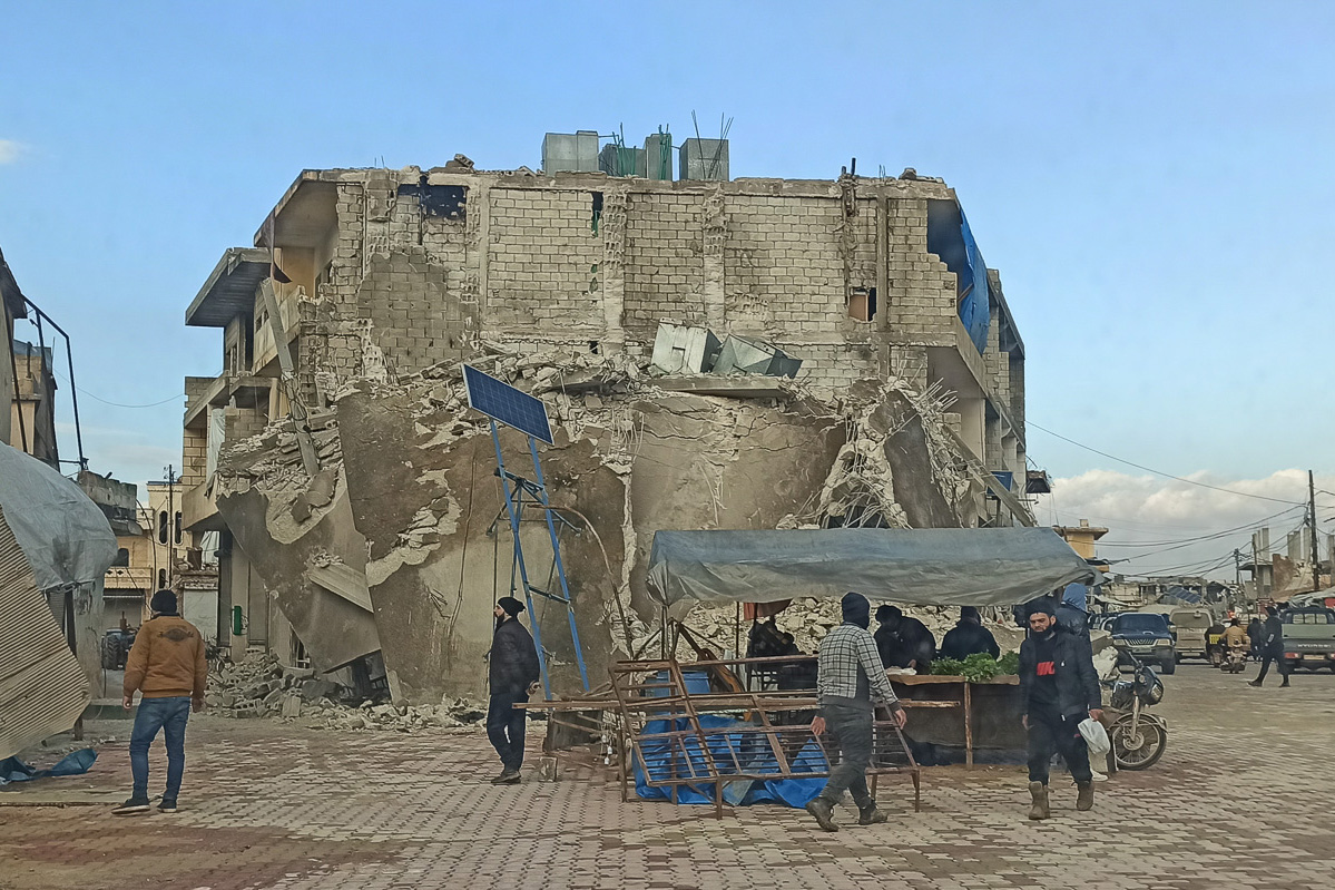 A market stall and people next to a badly damaged building