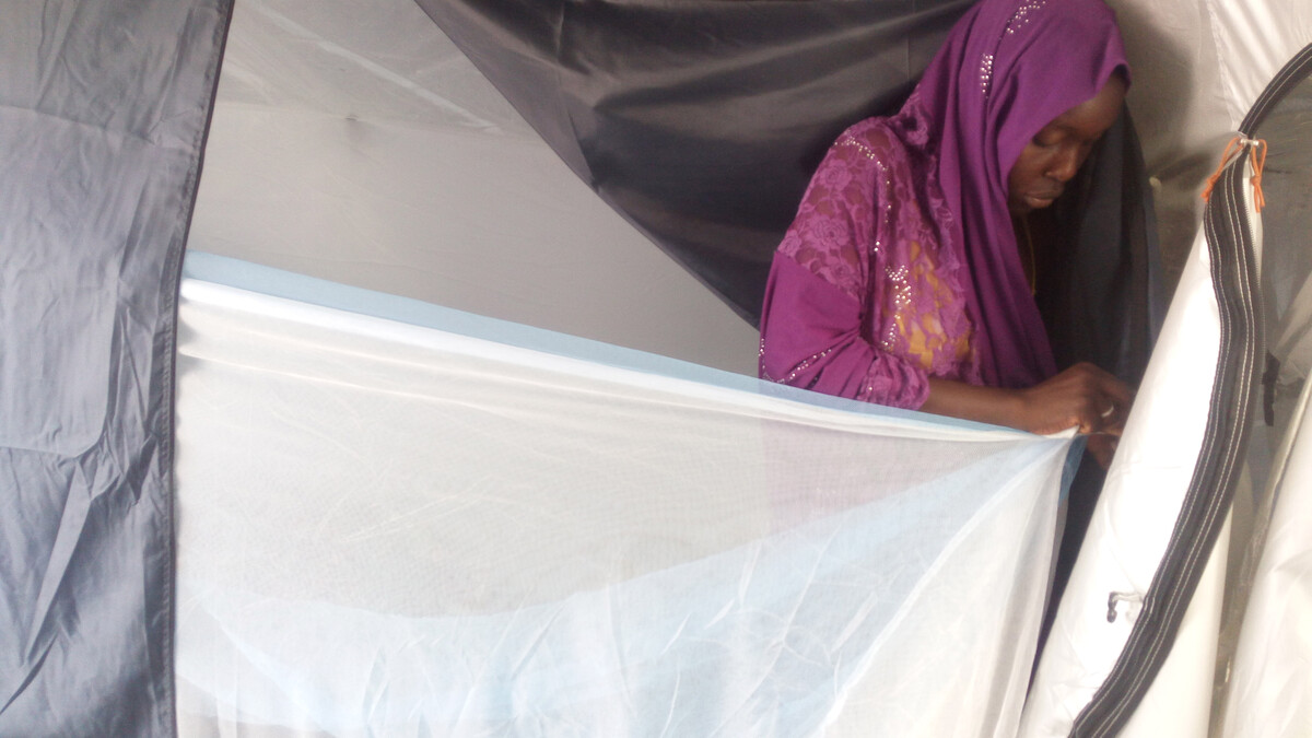Woman placing a mosquito net over the doorway of a tent