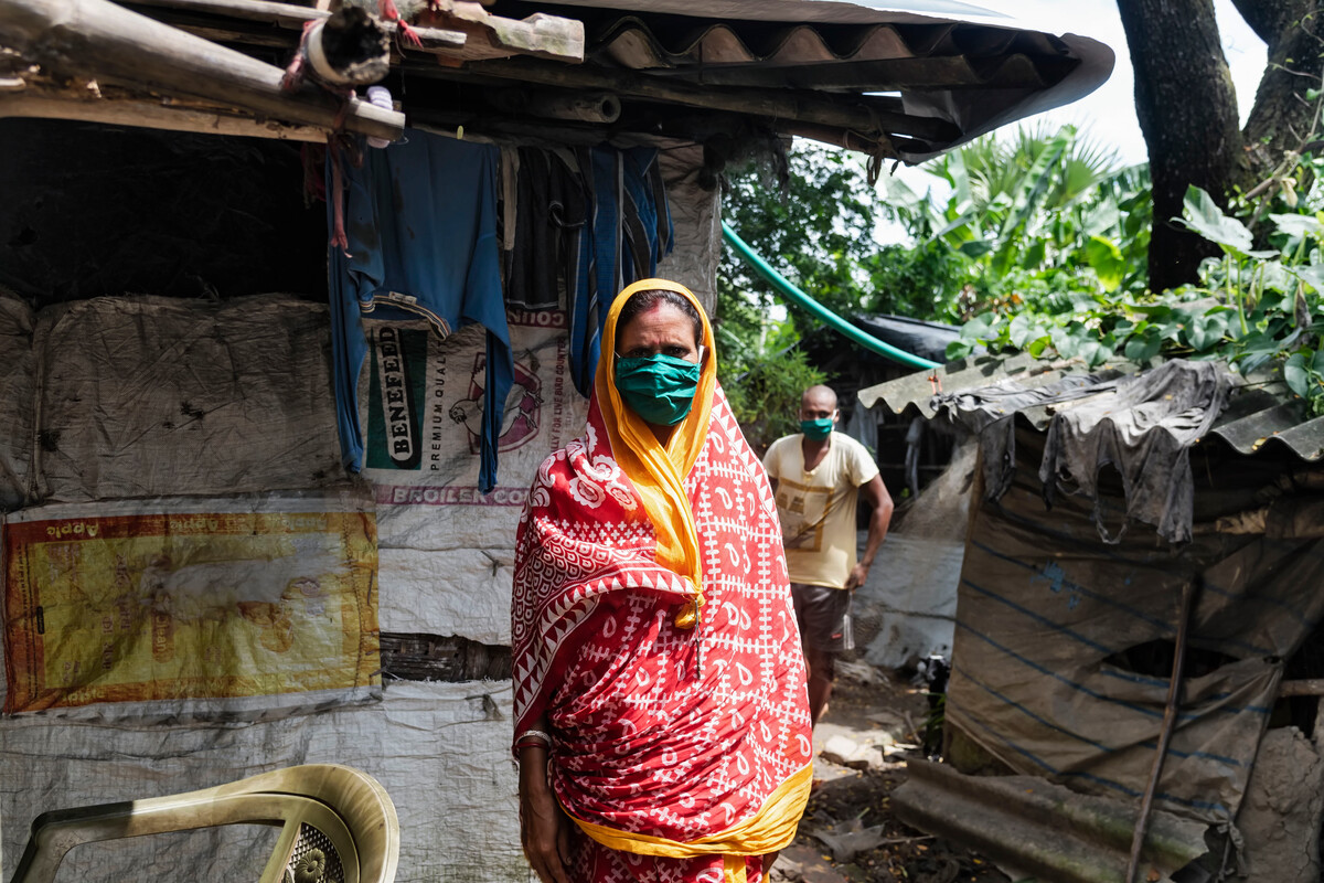 Woman in a colourful headscarf and wearing a face mask next to a shelter in India