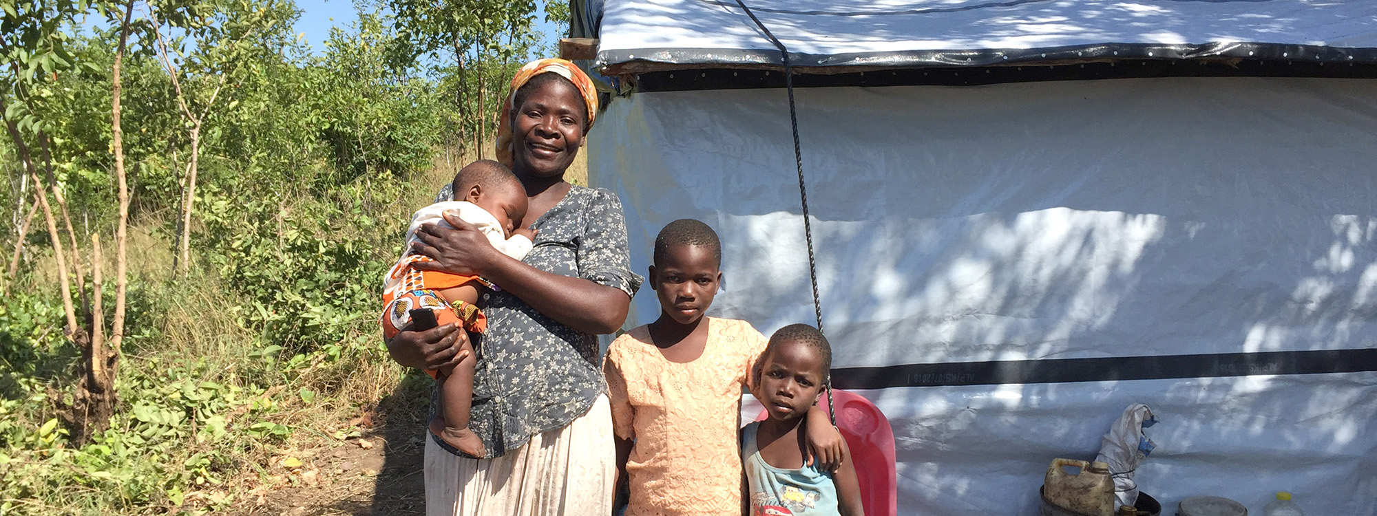 A mother and three children standing in front of a repaired shelter in Malawi