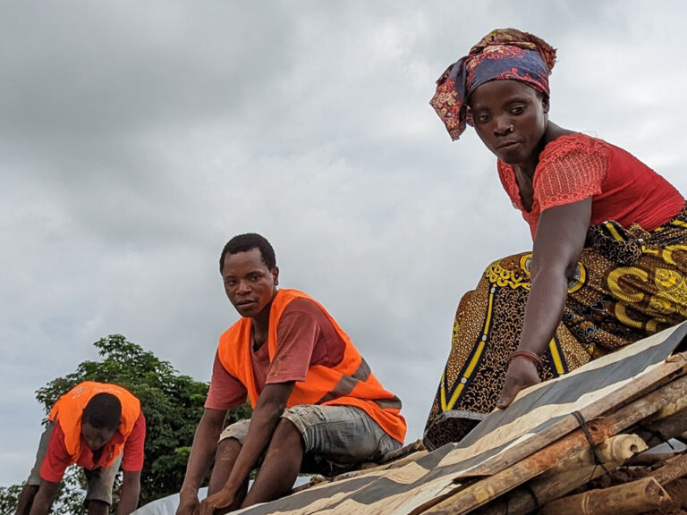 Three people finishing work on the roof of a new shelter in Mozambique