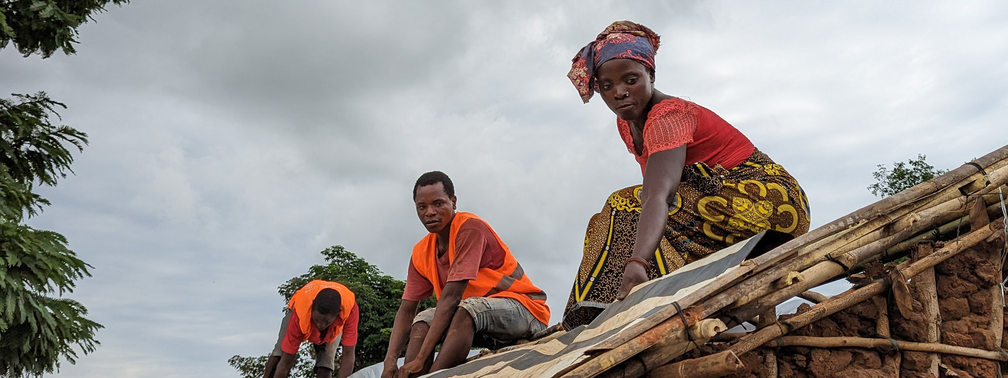 Three people finishing work on the roof of a new shelter in Mozambique