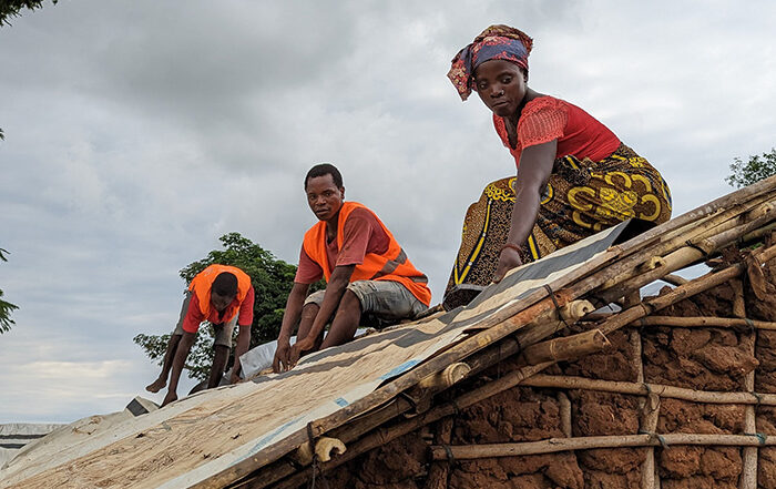 Three people finishing the roof of a new shelter in Mozambique