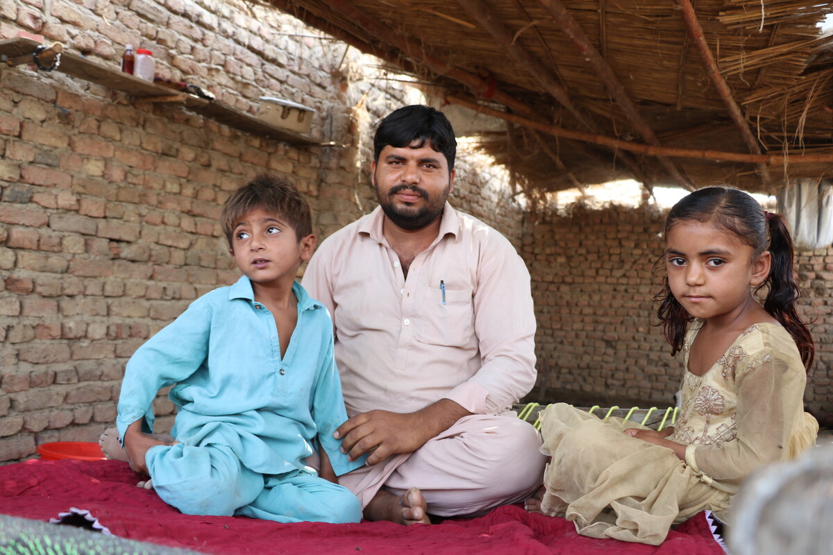 Man sitting on the floor with two children inside a shelter in Pakistan