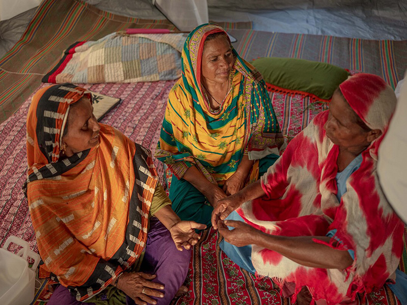 Three women in colourful headscarves sitting in a tent chatting in Pakistan