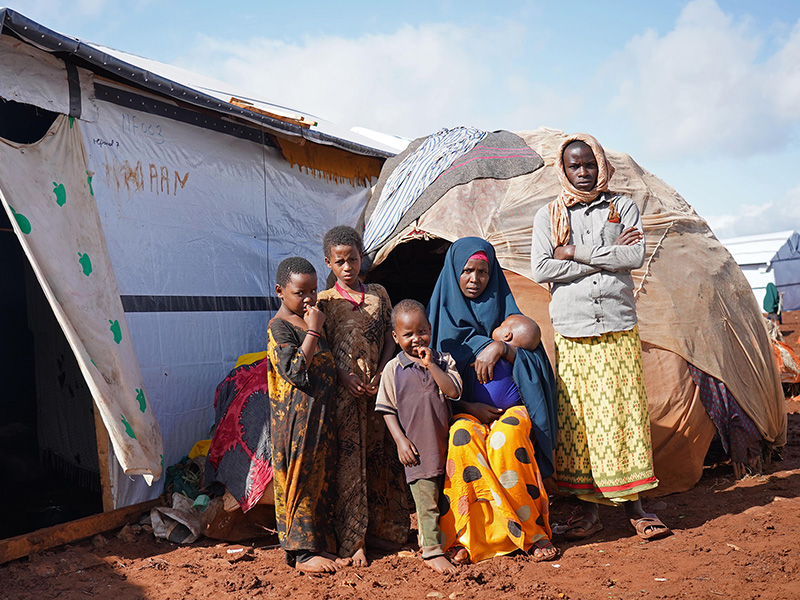 Family standing outside a small tent and larger shelter