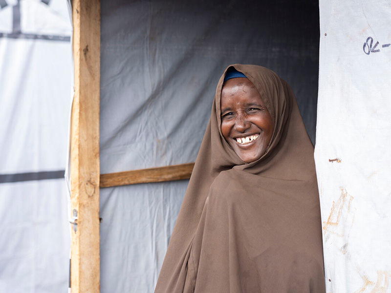 Lady in a brown headscarf smiling in the doorway of a new shelter in Somalia