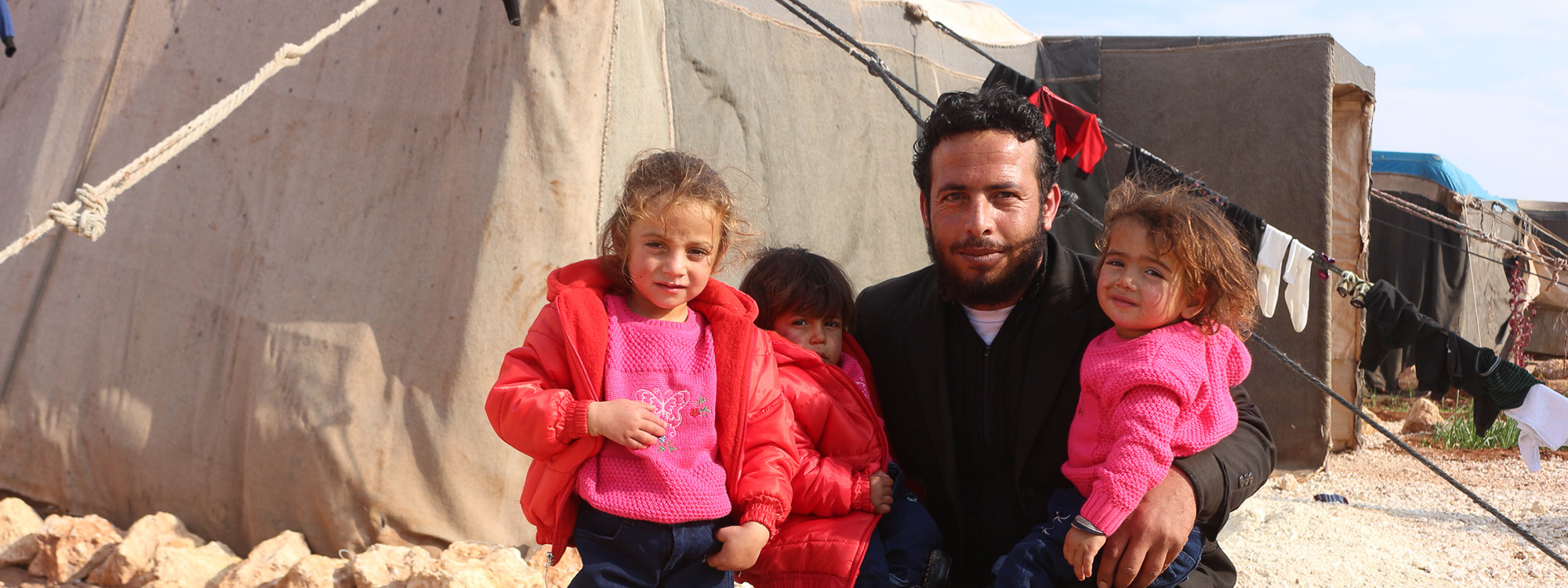 Man with three children next to a tent in Syria