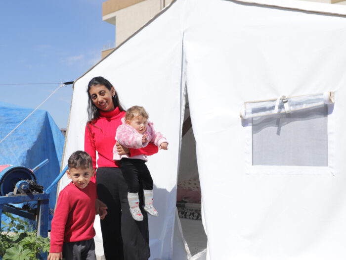 Woman holding a baby and the hand of a child next to a tent in Turkey