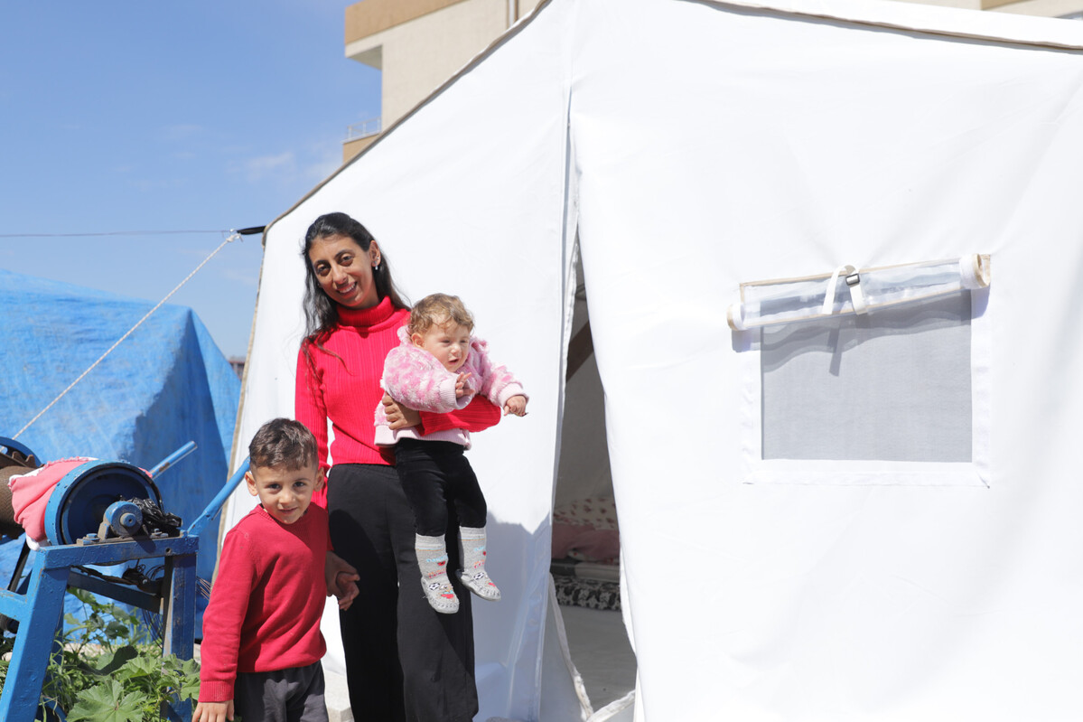 Woman holding a baby and the hand of a child next to a tent in Turkey