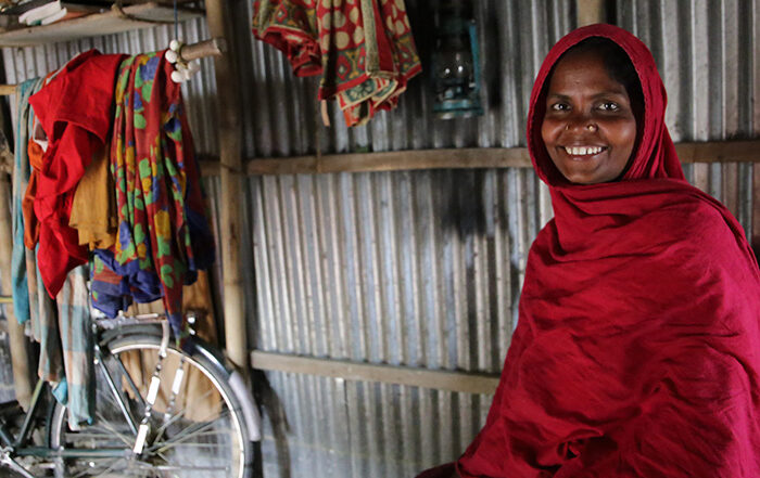 Woman wearing a head scarf smiling at the camera while inside a shelter in Bangladesh
