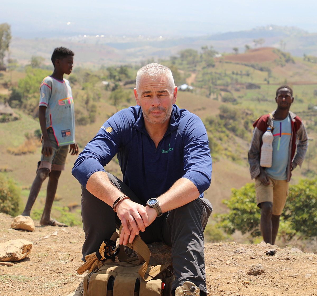 Man sitting with two children and the Ethiopian landscape behind him