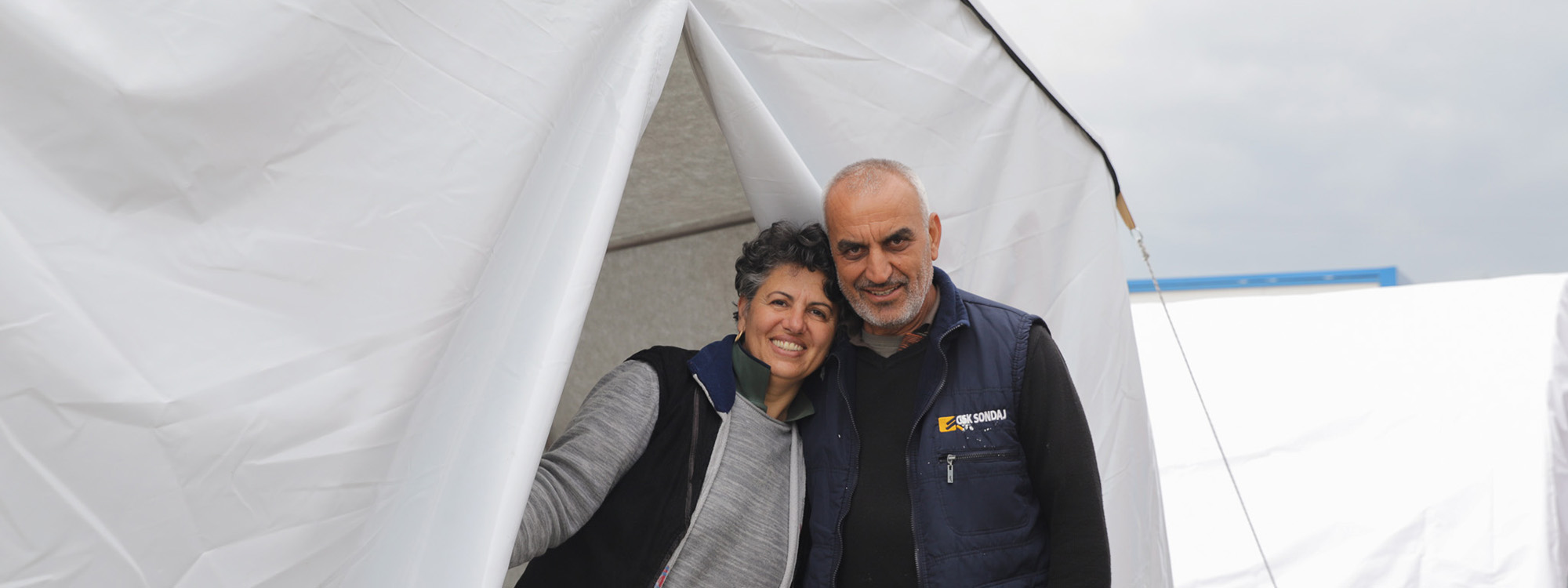 Man and woman standing in the door of a tent after losing their home to the Turkey earthquakes