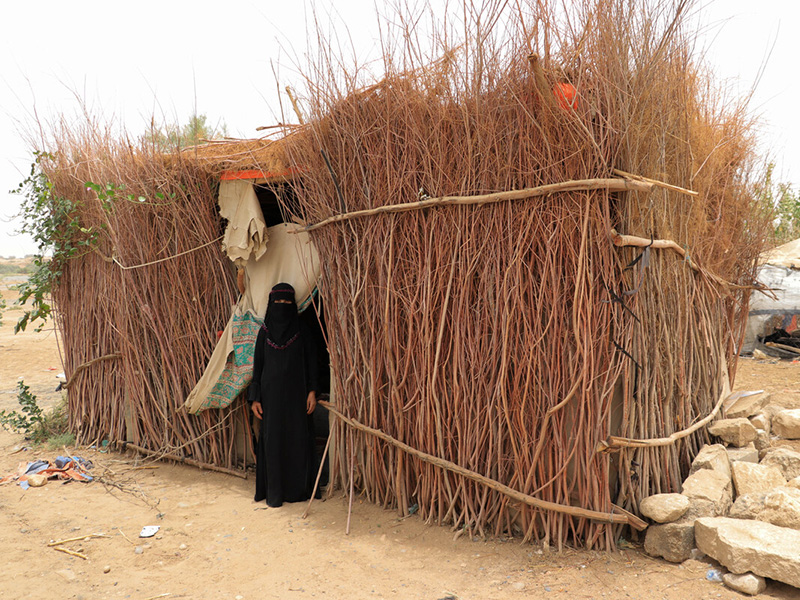 Woman standing outside a shelter made of thatched sticks in Yemen
