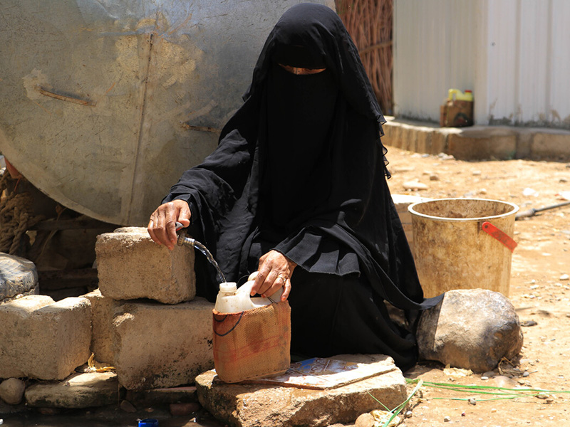 Woman filling a water carrier in Yemen