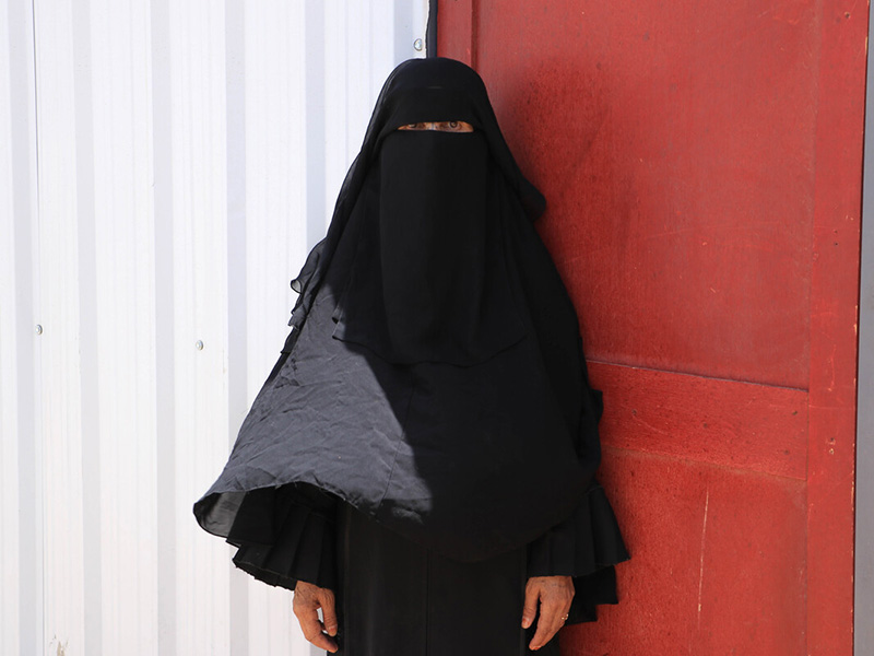 Woman standing next to a red door in Yemen