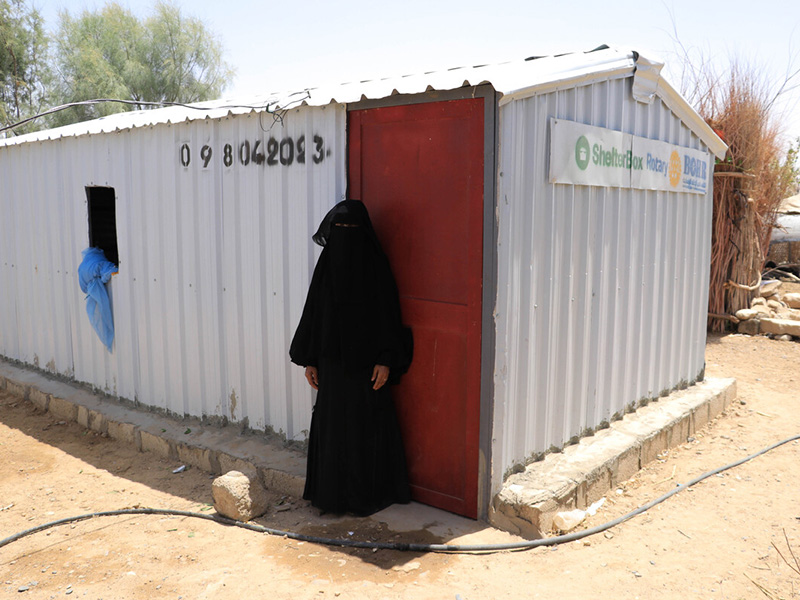 Woman standing in front of an iron net shelter in Yemen