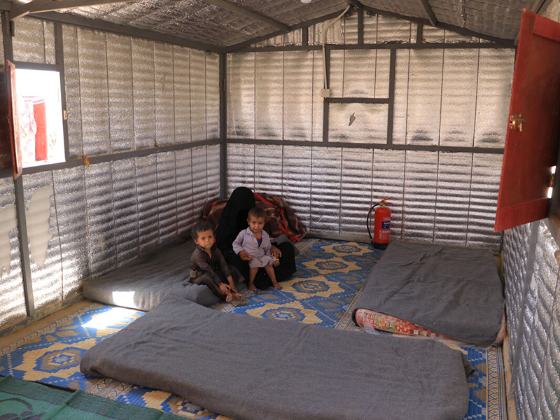Woman and two children sitting inside an iron net shelter in Yemen