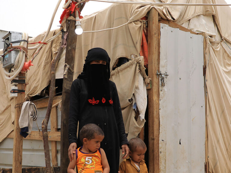 Woman and two children standing in front of a temporary shelter in Yemen