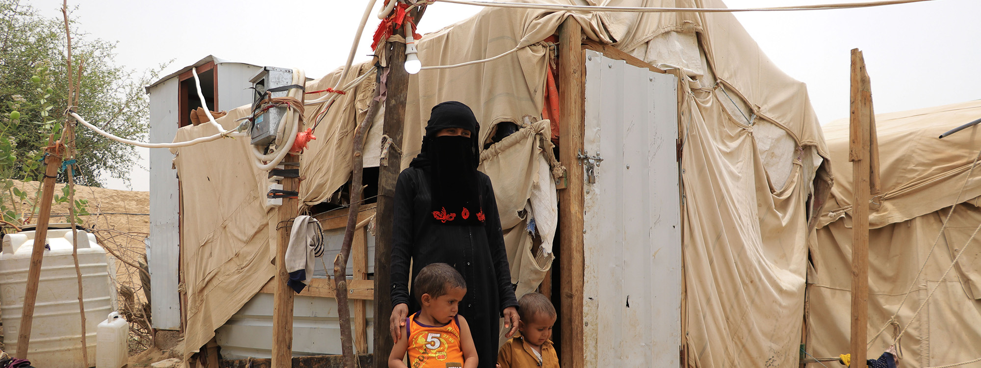 Woman and two children standing in front of a temporary shelter in Yemen