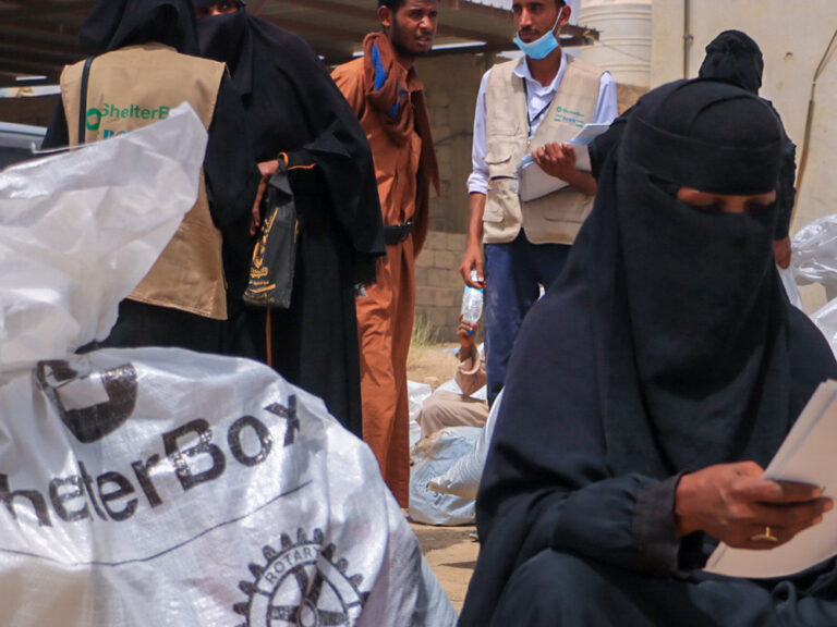 Woman reading a piece of paper sitting next to a bag of aid from ShelterBox in Yemen