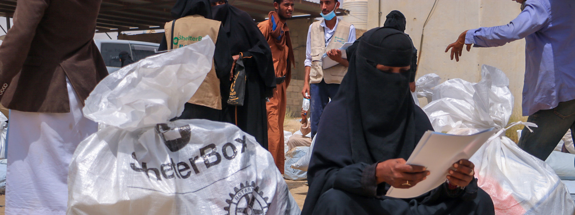 Woman reading a piece of paper sitting next to a bag of aid from ShelterBox in Yemen